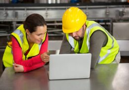 Male and female workers using laptop in factory
