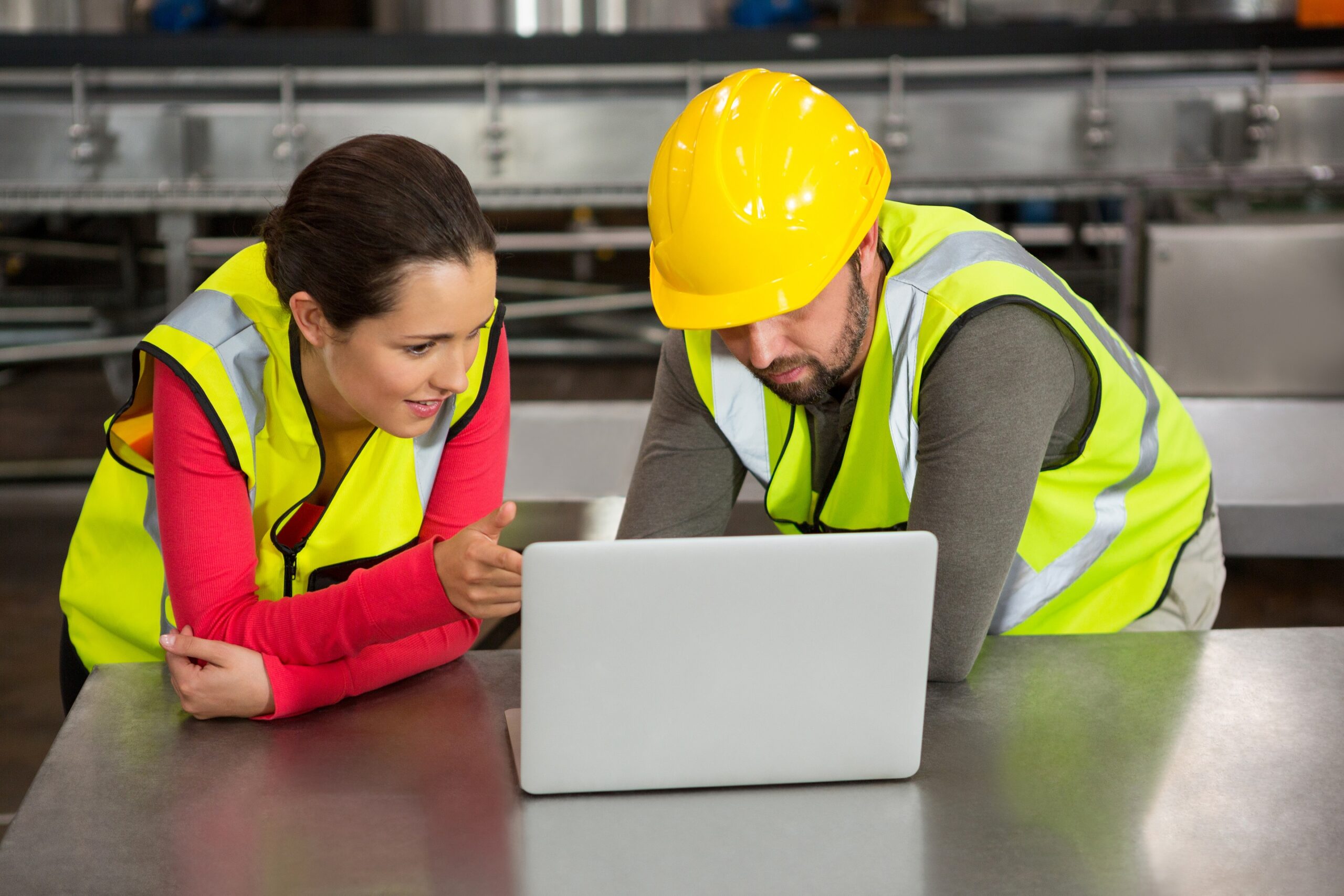 Male and female workers using laptop in factory