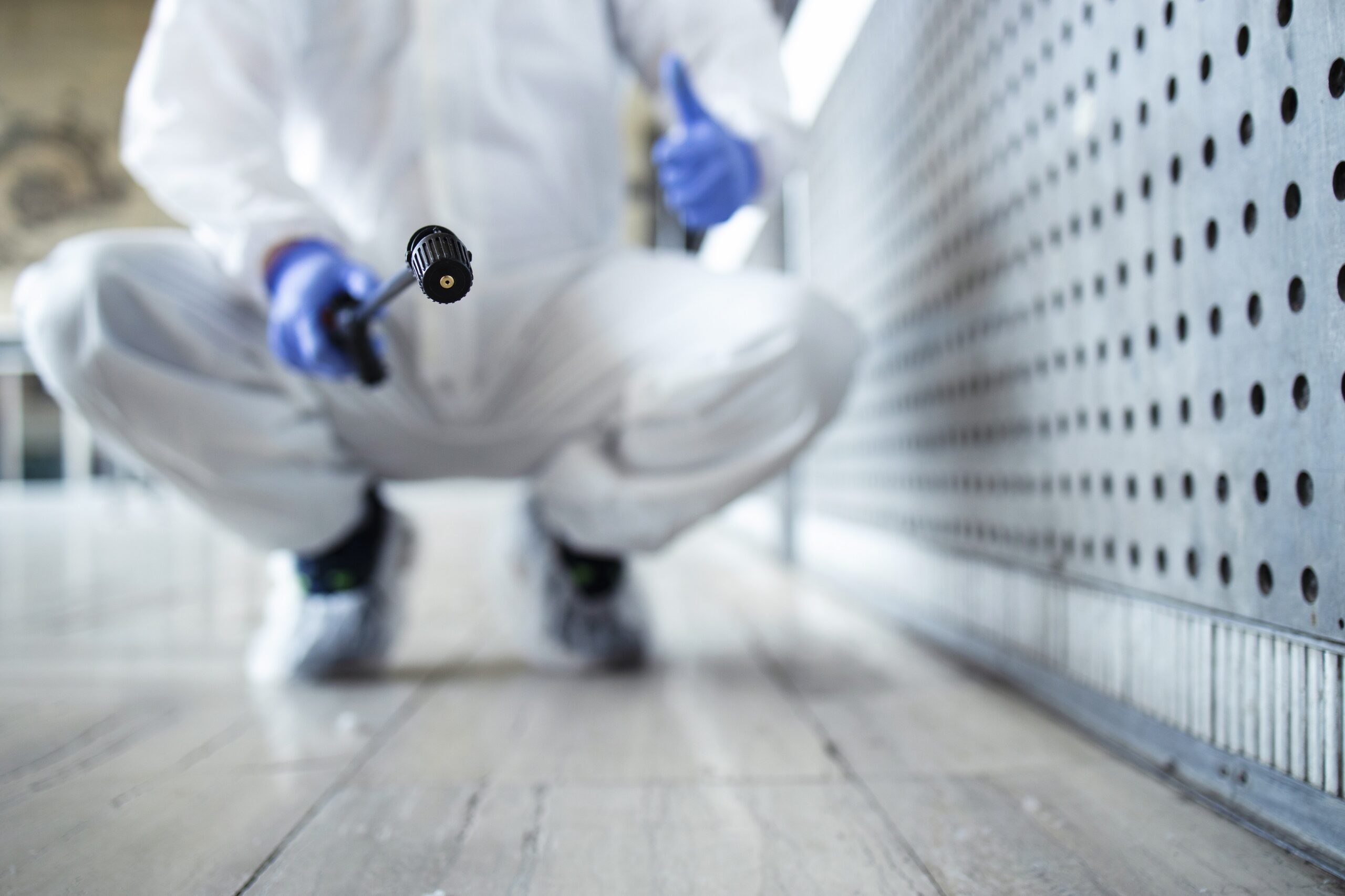 Unrecognizable person in white chemical protection suit doing disinfection of public areas to stop spreading highly contagious corona virus.